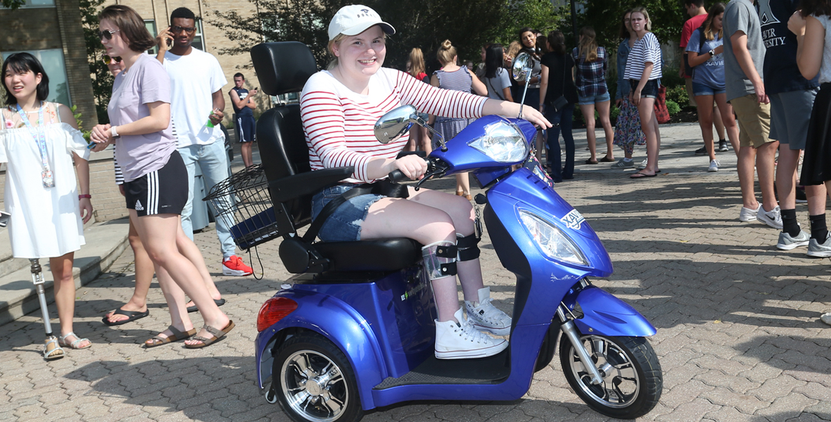 A Xavier student smiles at the camera while using their mobility scooter