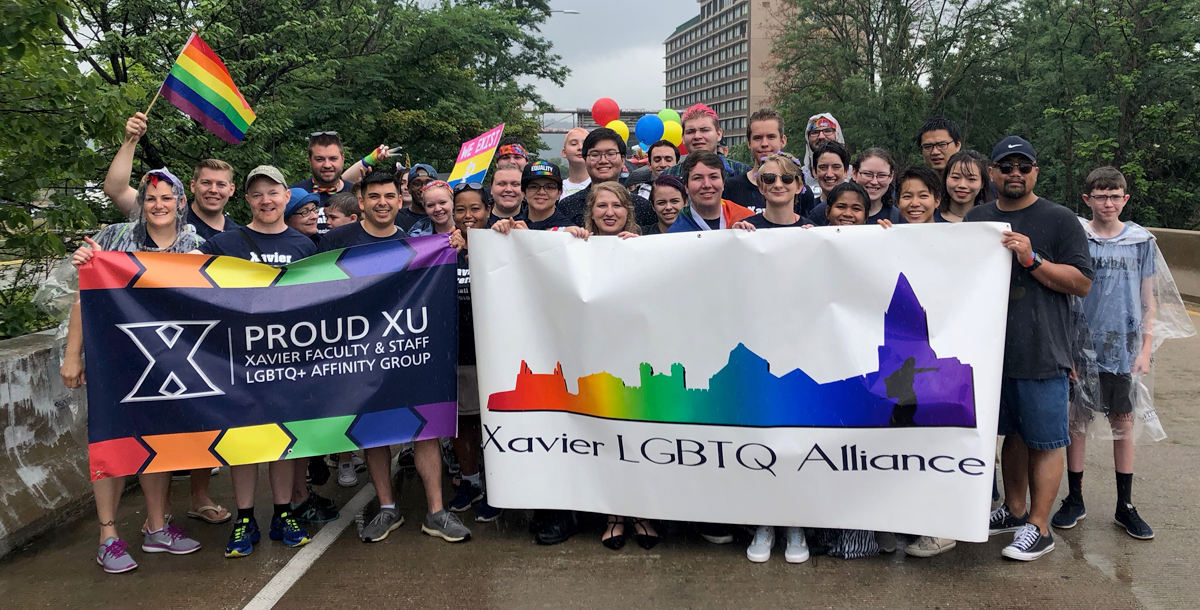 A group of Xavier students and alumni hold a Proud XU and Xavier LGBTQ Alliance flags