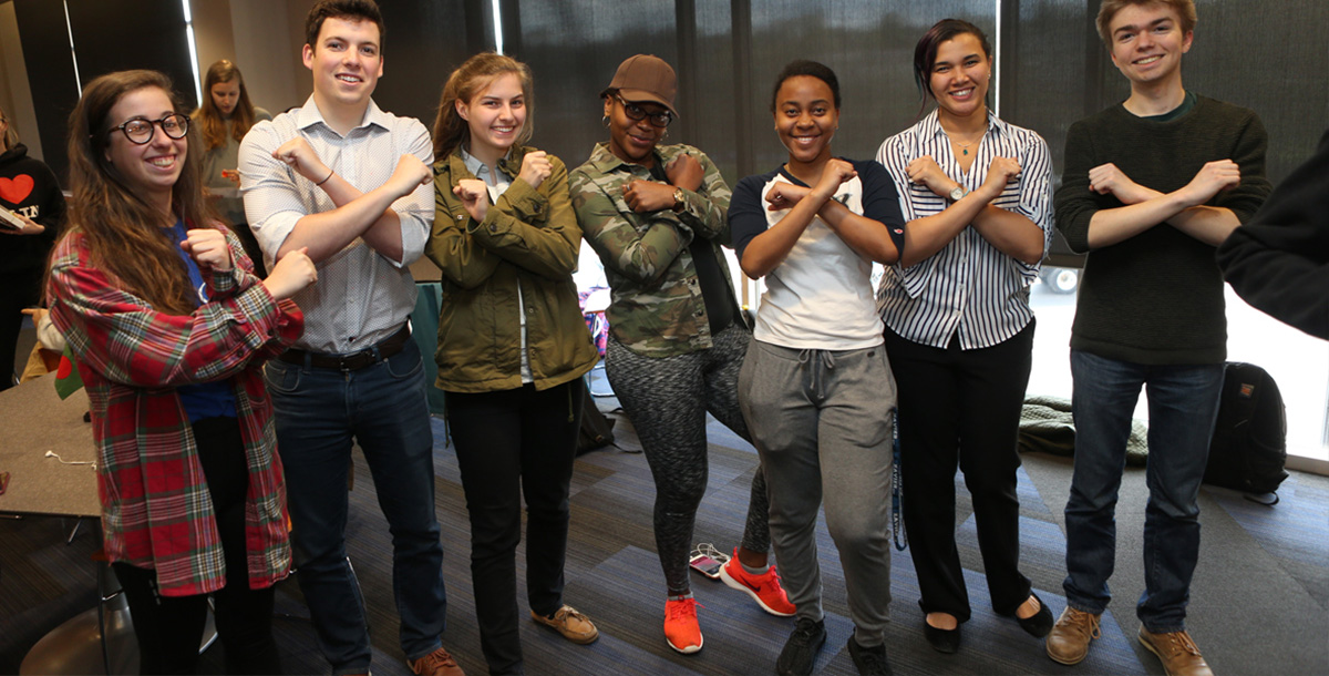 Seven Xavier students smile at the camera while forming an X shape by crossing their arms