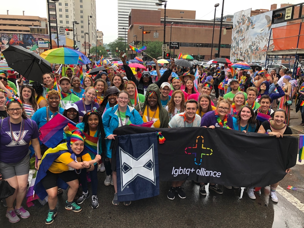 Xavier Students holding up a two banners, one is an Xavier flag and the other is an LGBTQ+ Alliance flag, while a taking picture during a rainy day out in Cincinnati