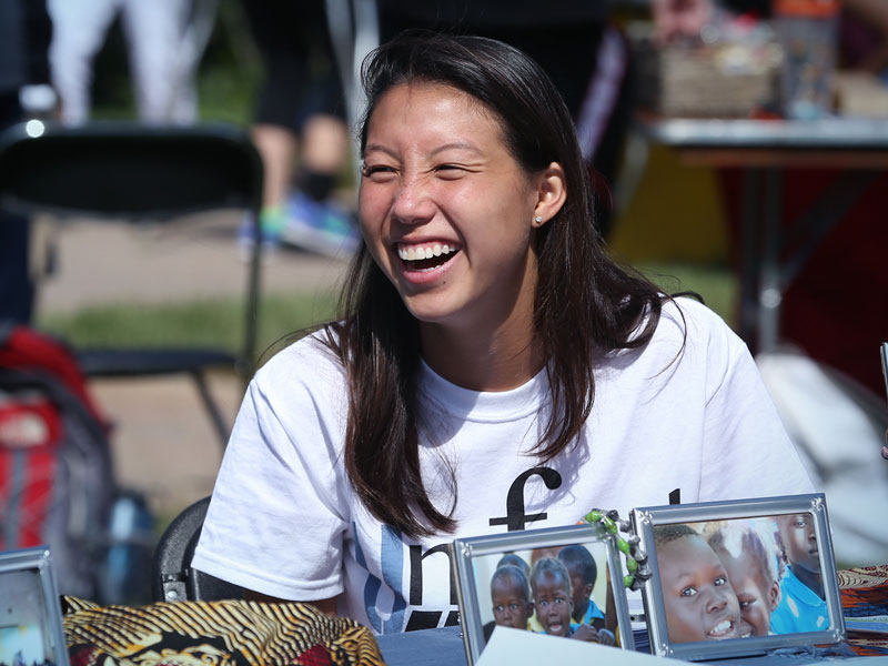 A Xavier student laughs while sitting down at an outdoor table in the summer.