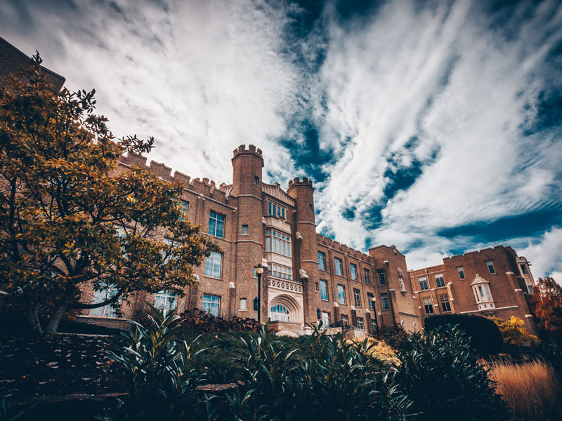 The exterior of Hinkle Hall. Hinkle Hall is a three-story building designed in a Tudor-Gothic style. is a The sky is bright blue with whispy clouds. 