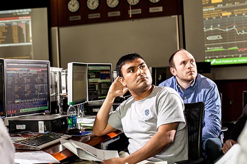 Two students sitting in front of computers with graphs on them