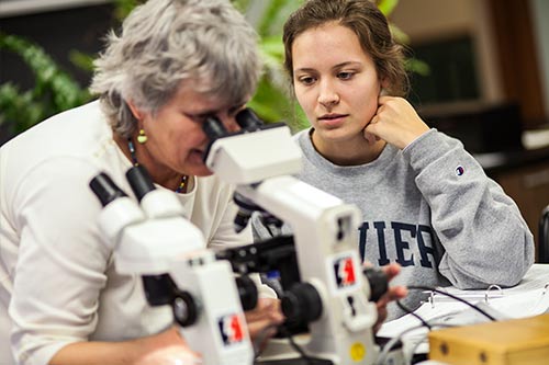 Student watching a professor use a microscope