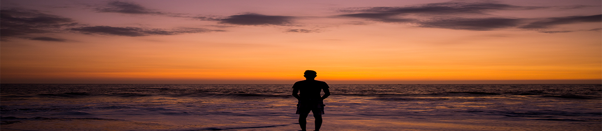 a man standing in front of an ocean at sunset