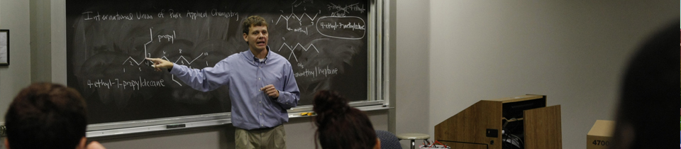 Photo of Professor Giving his Class a Lecture with Chalkboard Writing Behind him