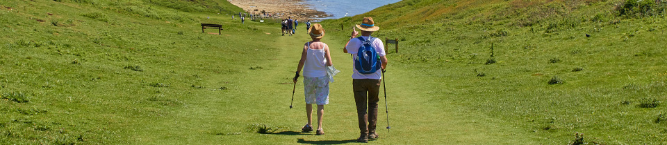 An elderly couple hiking on a grassy path to the beach