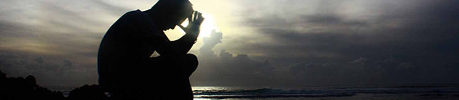 A man bowing his head in prayer on a beach