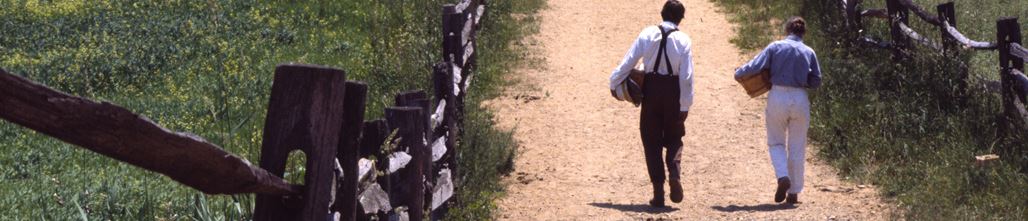 Two men carrying baskets walking down a dirt path