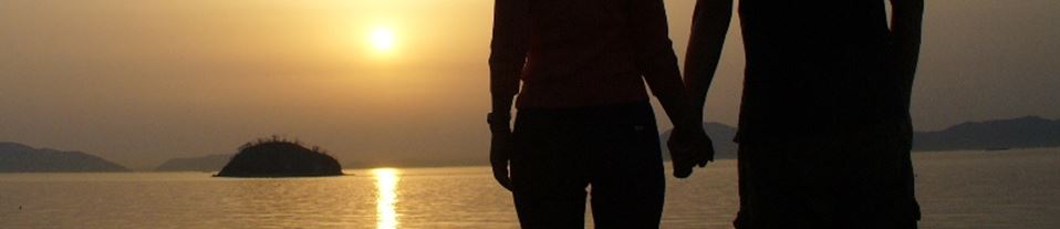 Photo of a couple holding hands in front of a sunset on a lake