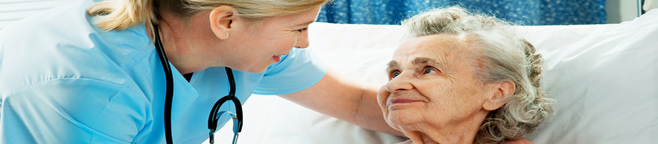 A nurse smiling at an elderly patient in a hospital bed