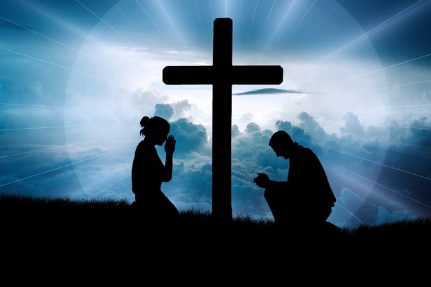 Two silhouettes kneeling before a cross