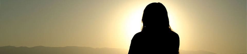 Woman standing in front of the sun in a mountain range