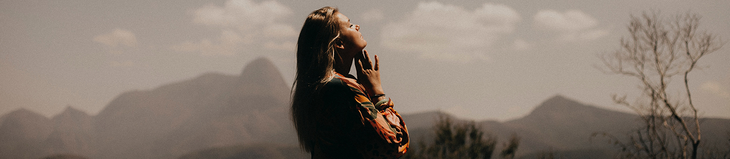 Photo of a woman praying with her head to the sky in the desert with mountains in the background