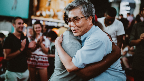 Two people embrace as a crowd watching them applauds