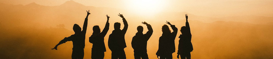 Silhouettes of a group of friends holding up peace signs in front of a sunset