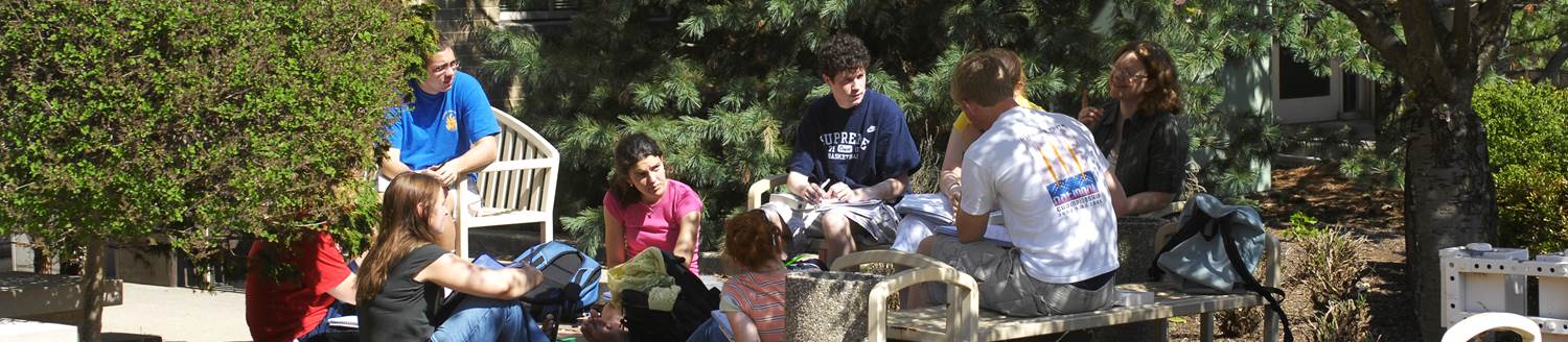 Group of people gathered outside sitting on the ground and on benches