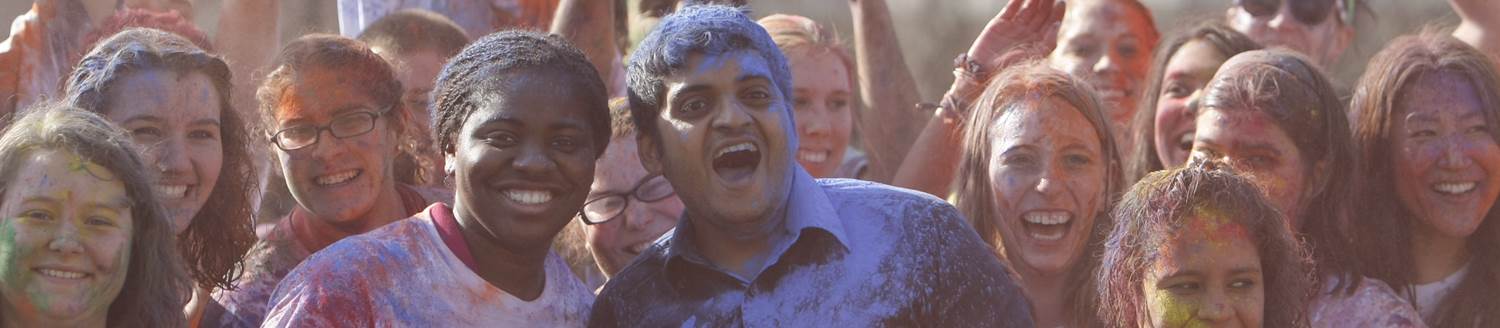 Photo of a group of people of different races, genders, and backgrounds all smiling together in colored powder