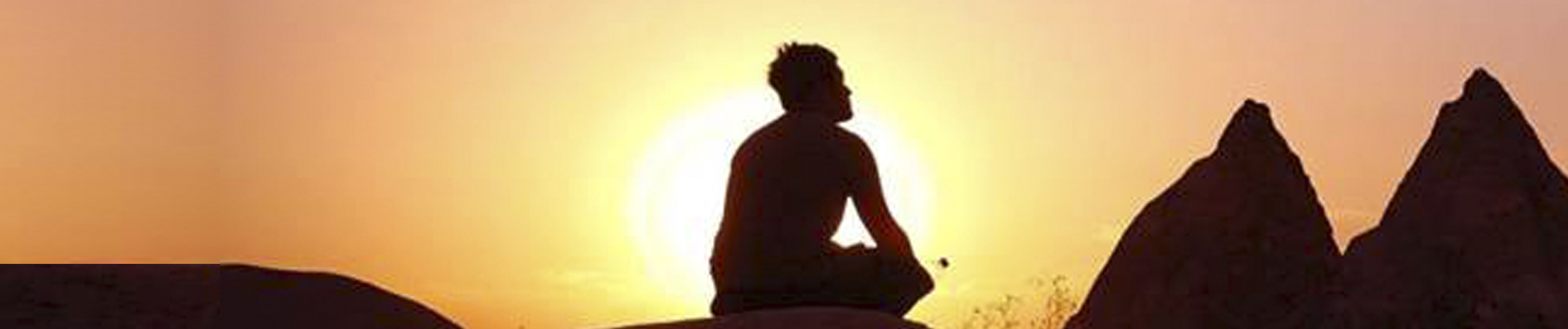 Photo of person sitting on hill in front of a sunset meditating