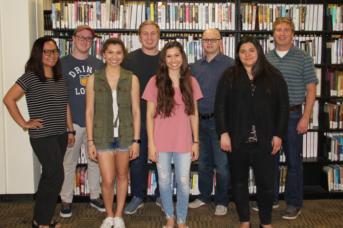 Group of seven adults smiling together in front of a row of bookshelves in a library