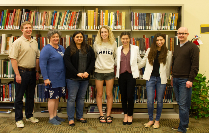 Group of six adults smiling together in front of a row of bookshelves in a library