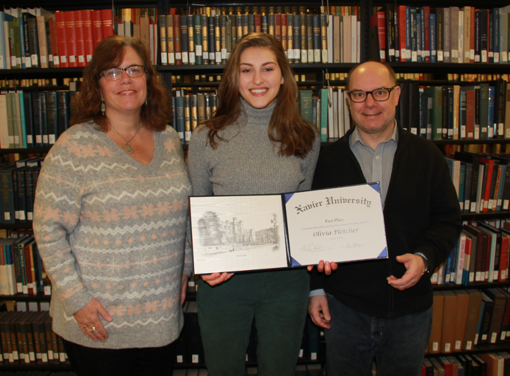 Assistant Library Director Alison Morgan, Olivia Pletcher, and Don Prues smiling together in front of an aisle of books in the Xavier University Library