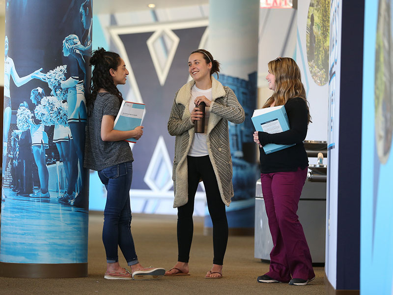 Three Xavier students are holding their books and talking with each other in the Health United Building