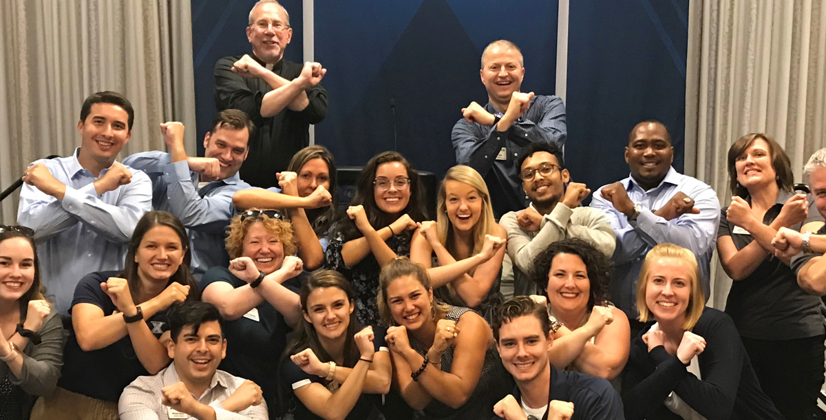 A group of about twenty Xavier admission counselors gather together for a group photo. Everyone is crossing their arms to form an X.