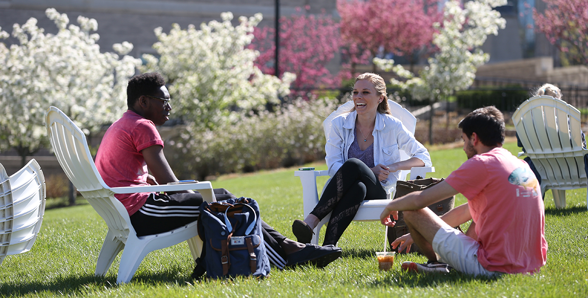 Three Xavier students sitting outside on white Adirondack chairs in the springtime 