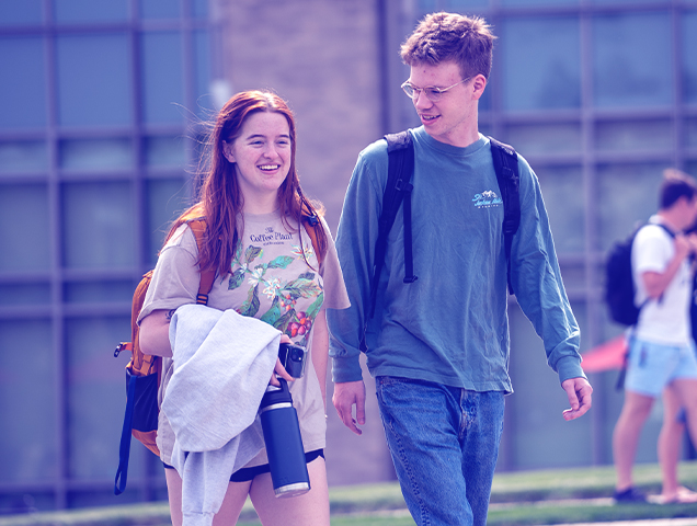 Two students walking across campus holding their cell phones
