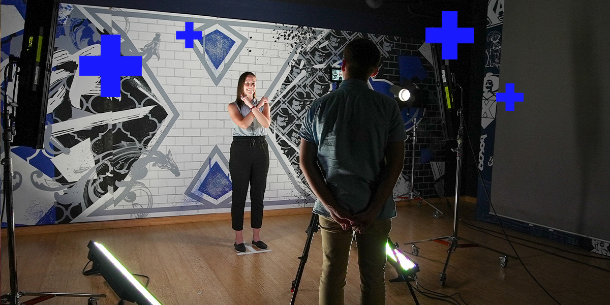 A Xavier employee stands in front of a Xavier logo backdrop and poses to have their portrait taken