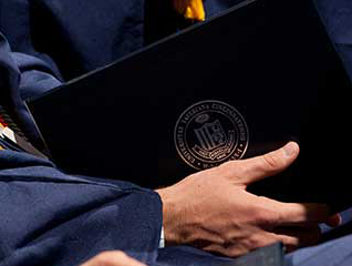 Graduate in their commencement gown holding their physical degree