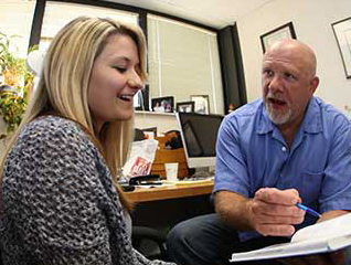 Professor explaining something to a student while pointing out the concept in a textbook