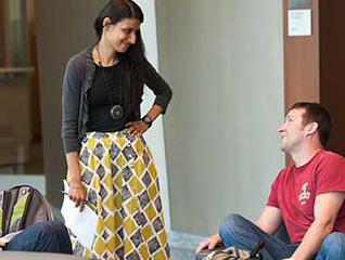 A student sits cross legged on the ground while an educator stands beside them