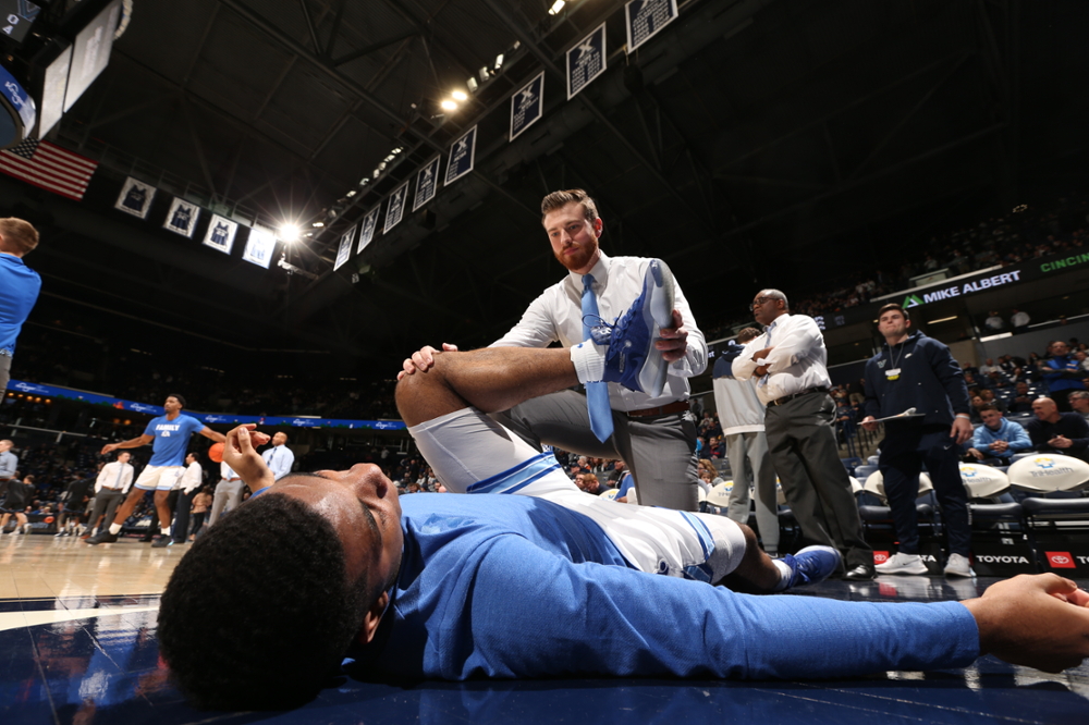 Low-Angle photo of an Athletic trainer helping a fellow Athlete stretch