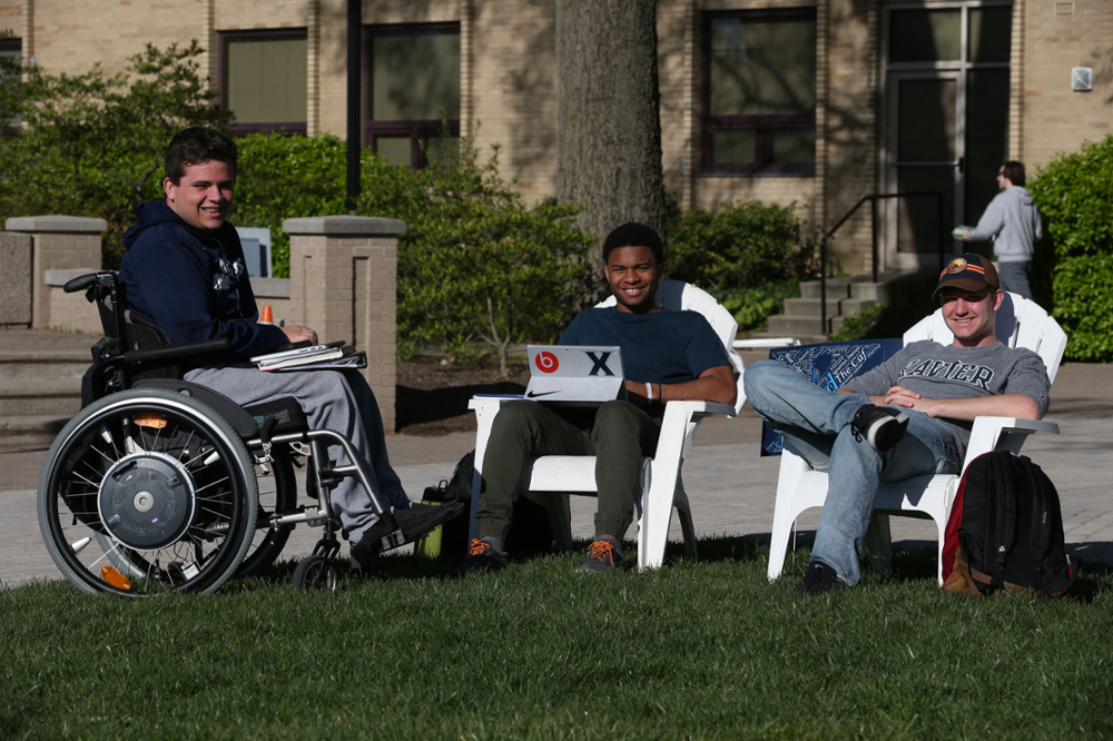 Three Xavier students sitting in white lawn chairs outside Husman Hall