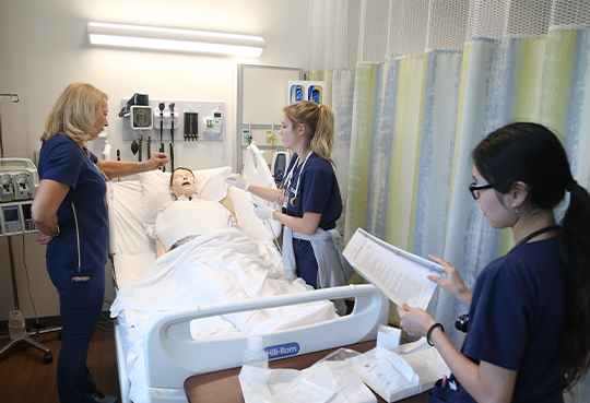 Two Xavier students learn bedside care from a nursing instructor in a nursing simulation lab
