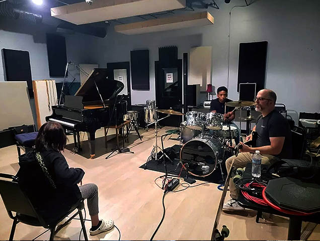 A group of students playing instruments in a studio room with a professinal.