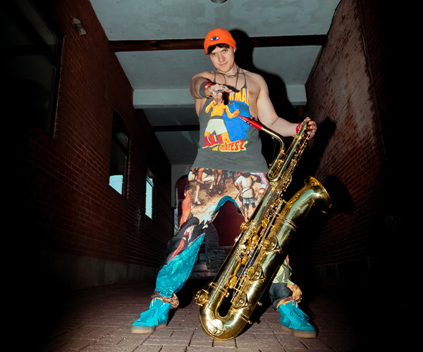 Michael Wilbur holding a saxophone and posting towards the camera