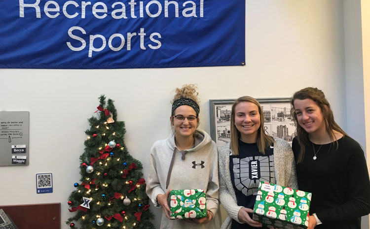 Three softball players with donated items they helped wrap. 