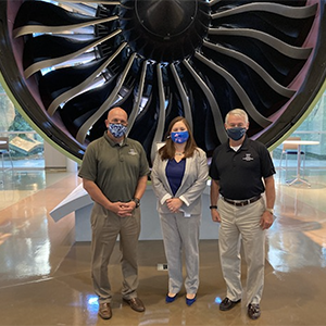 Three individuals standing in front of an engine at G.E. Aviation headquarters