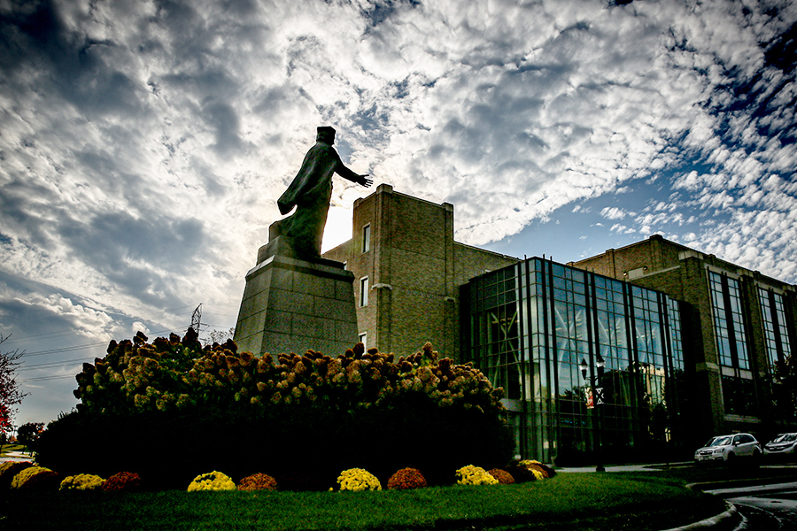 Photo of the St. Francis Xavier statue located on St. Francis Xavier Way on campus. Smith Hall is in the background. 