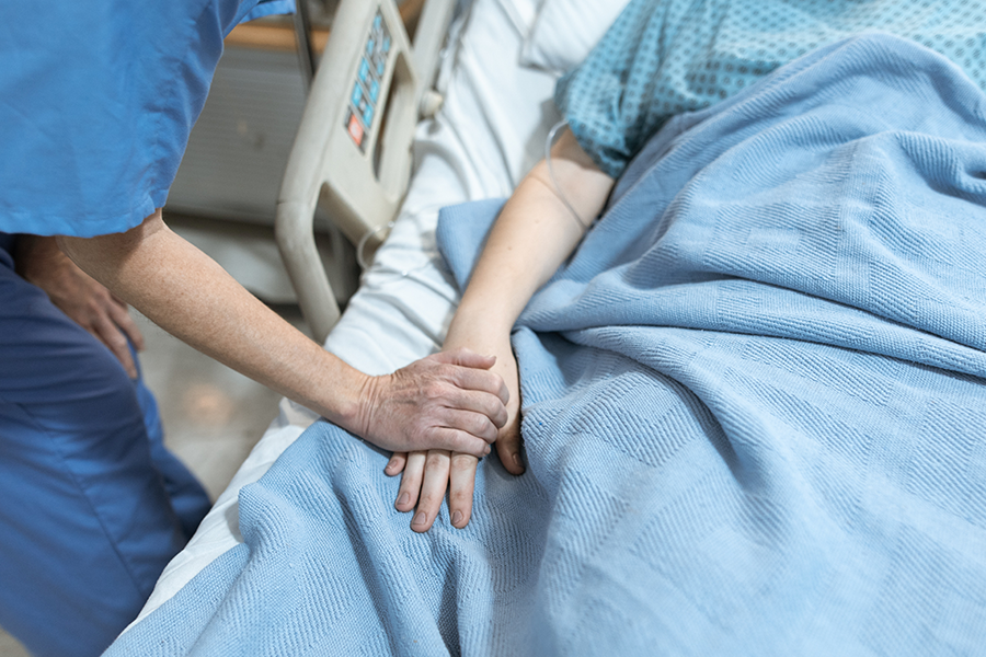 A medical professional holding the hand of someone in a hospital bed