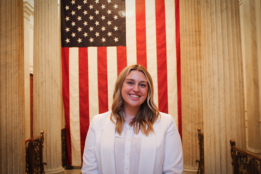 Xavier senior Abby White poses in front of a large American flag hanging on the wall behind her.