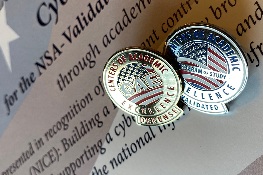 Two ceremonial pins reading rest on a certificate recognizing Xavier University for its excellence in cyber defense