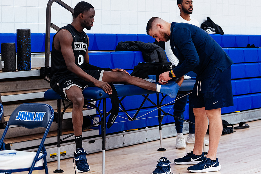 Xavier alum Connor Barnes tapes up an athlete's ankle. Athlete is sitting on a blue bench. 