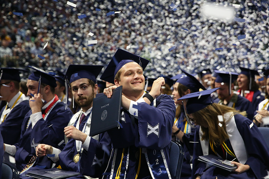 Confetti falls as Xavier graduates dressed in cap and gown applaud, with one making an X symbol with his arms, during the 2023 spring commencement ceremonies.