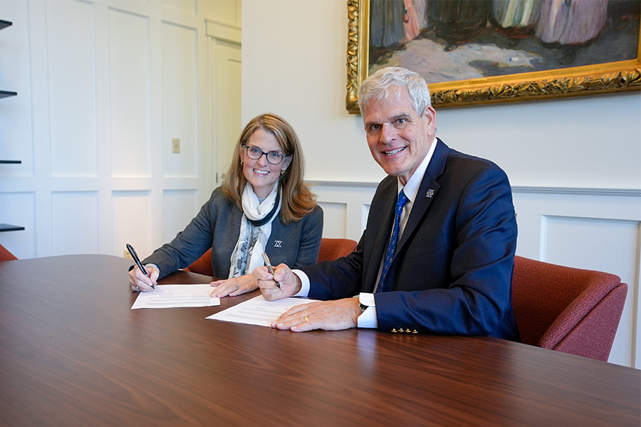 Xavier University President Dr. Colleen Hanycz and President of St. Xavier High School Tim Reilly hold pens with paperwork sitting on the desk in front of them.