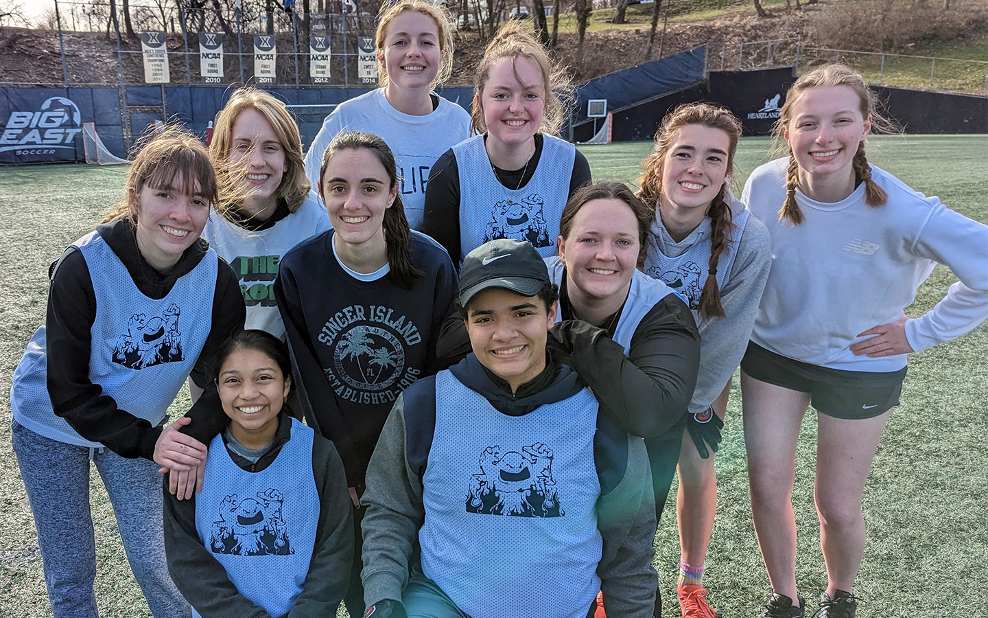 Sydney sits at the center of a team picture of some members of the Women's Ultimate Frisbee team wearing practice pennies on a field