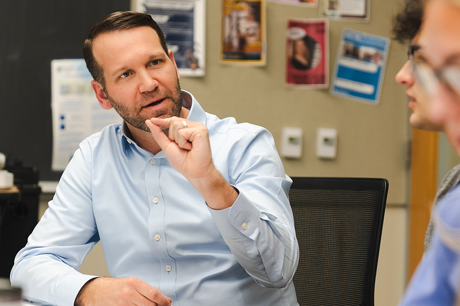 Professor Randy Brown pinches his fingers together while speaking to students at a table.